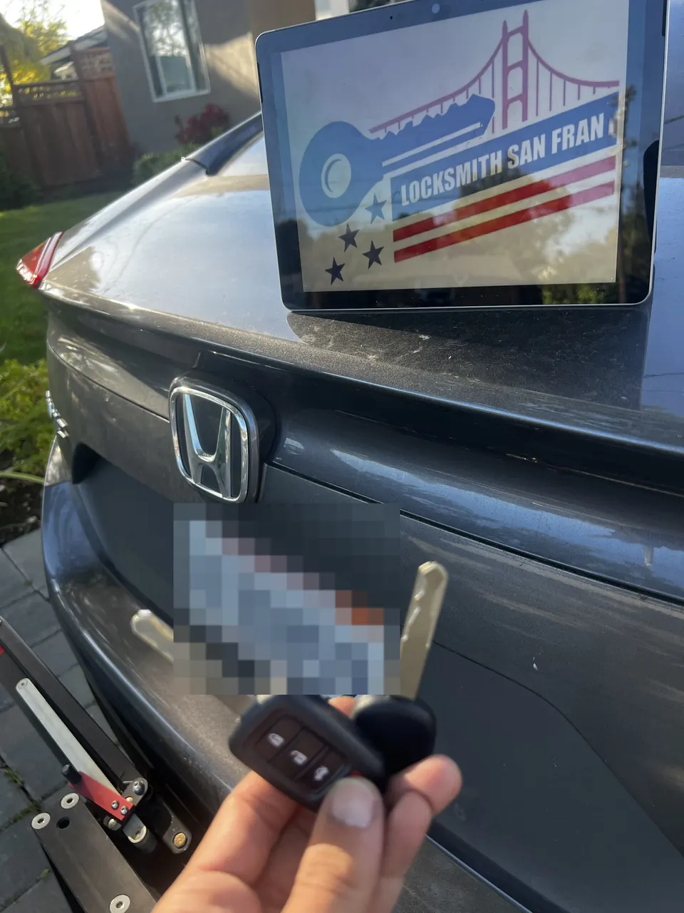 A newly cut flip key held up at the back of a Honda.