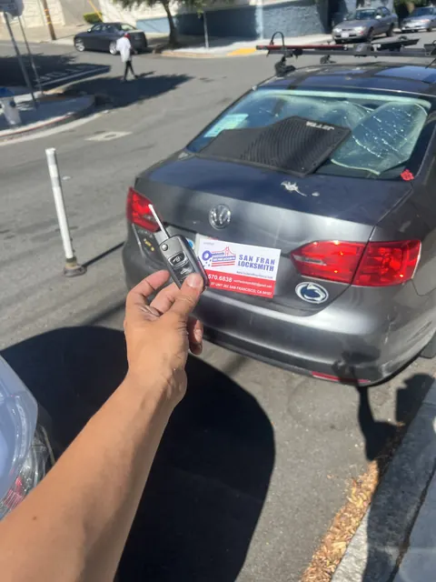A new key held at the rear of a Volkswagen Jetta parked on a hill, company sign on the trunk.