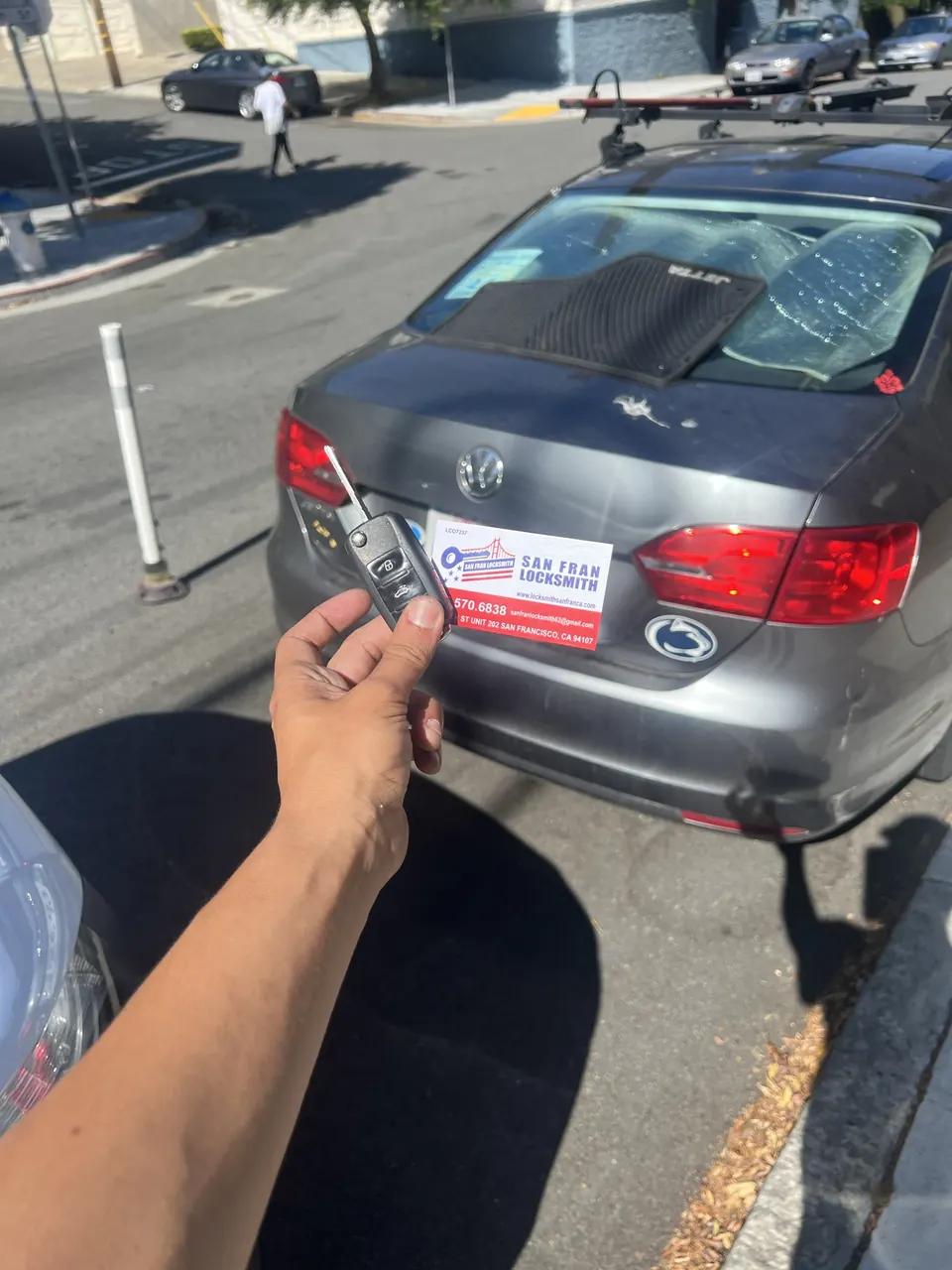 A new key held at the rear of a Volkswagen Jetta parked on a hill.